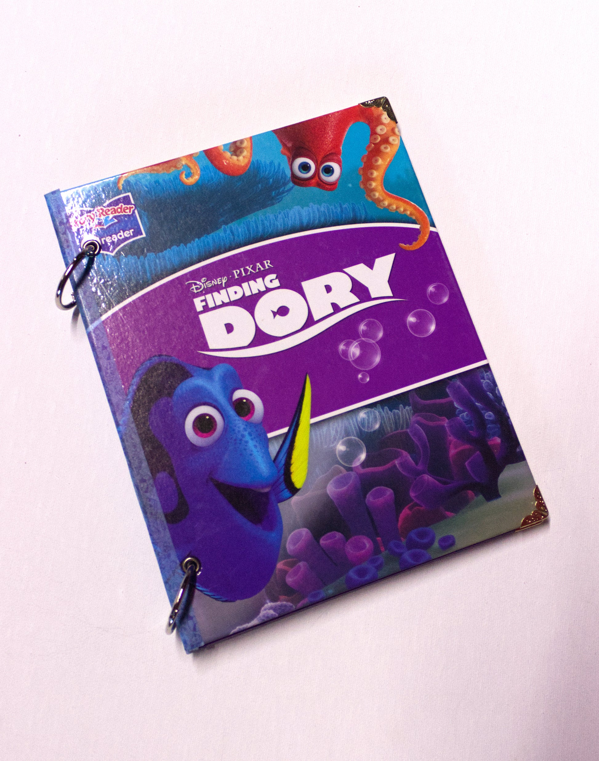 Upcycled children’s book journal made from a Finding Dory hardcover, featuring a colorful ocean scene with animated fish characters, metal ring binding, and reinforced corners.
