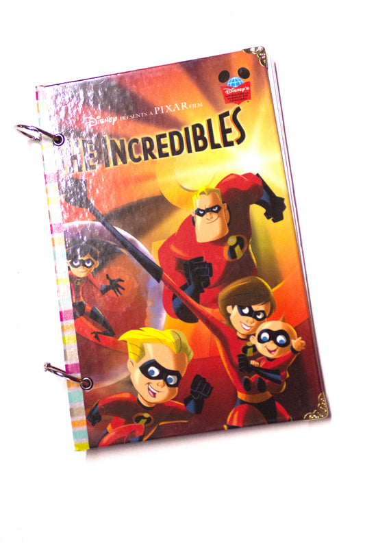 Upcycled children’s book journal made from a The Incredibles hardcover, featuring colorful superhero characters on the cover, bound with metal rings and reinforced corners.
